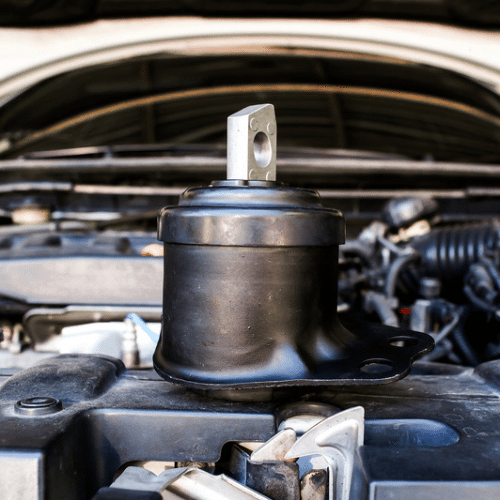 A black engine mount placed on top of a car engine with the car hood open in the background, illustrating a typical step during Mazda repair or maintenance.