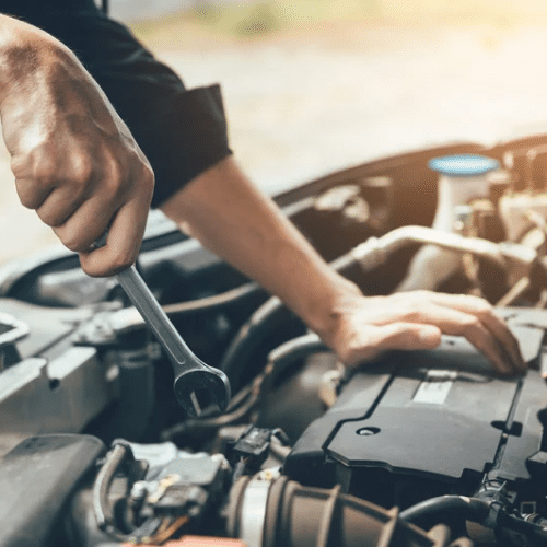 Person performing Mazda maintenance using a wrench to work on a car engine with the hood open.